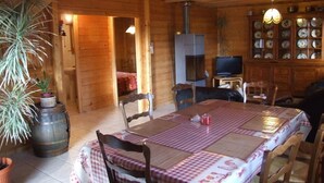 Ein Holzblockhaus-Interieur mit Esstisch, Stühlen, Kamin und Fernseher.