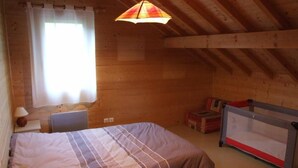 Ein gemütliches Zimmer mit einem Bett, einem Schreibtisch, einer Lampe, einem Fenster mit Vorhängen und einer Pendelleuchte.