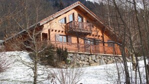 Eine Holzhütte mit Balkon, auf einem Steinfundament gelegen, umgeben von Schnee und Bäumen.