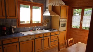 Eine kleine Küche mit Holzschränken, einer Spüle, einem Herd und einem Fenster mit Blick auf einen Garten.