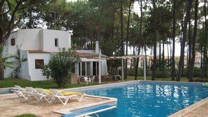 A swimming pool with lounge chairs, a covered seating area, and a white building with a tiled roof. - Luxury villa with large garden and pool, next to the golf course and near the beach (Vilamoura)