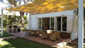 An outdoor patio with a barbecue, wicker furniture, and a covered area with yellow canopies. - Luxury villa with large garden and pool, next to the golf course and near the beach (Vilamoura)