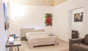 A bedroom with a bed, bedside tables, a lamp, and a painting of cherries. - Ailanthus Holiday Suites (Polignano a Mare)