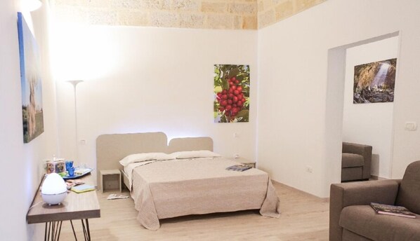 A bedroom with a bed, bedside tables, a lamp, and a painting of cherries. - Ailanthus Holiday Suites (Polignano a Mare)
