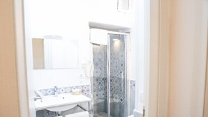 A bathroom with a sink, mirror, and shower with patterned tiles. - Ailanthus Holiday Suites (Polignano a Mare)