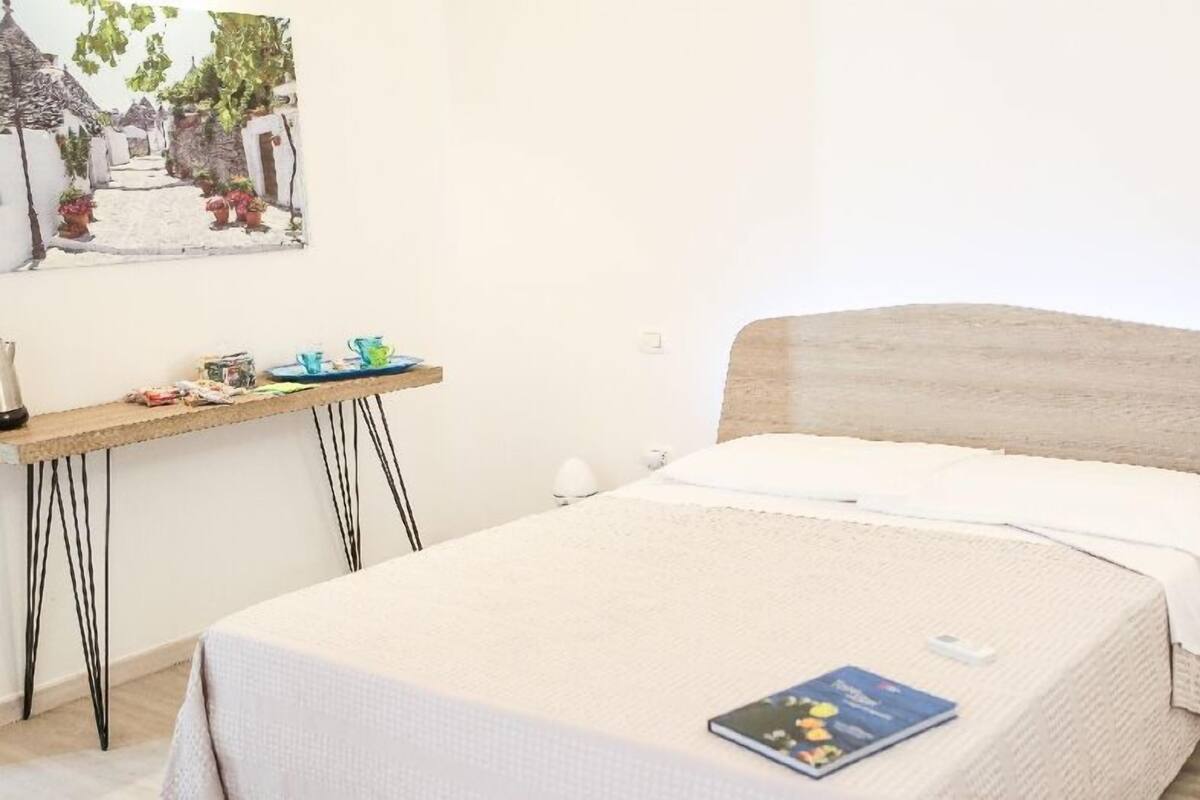 A bedroom with a bed, a small desk, a chair, and a painting on the wall.