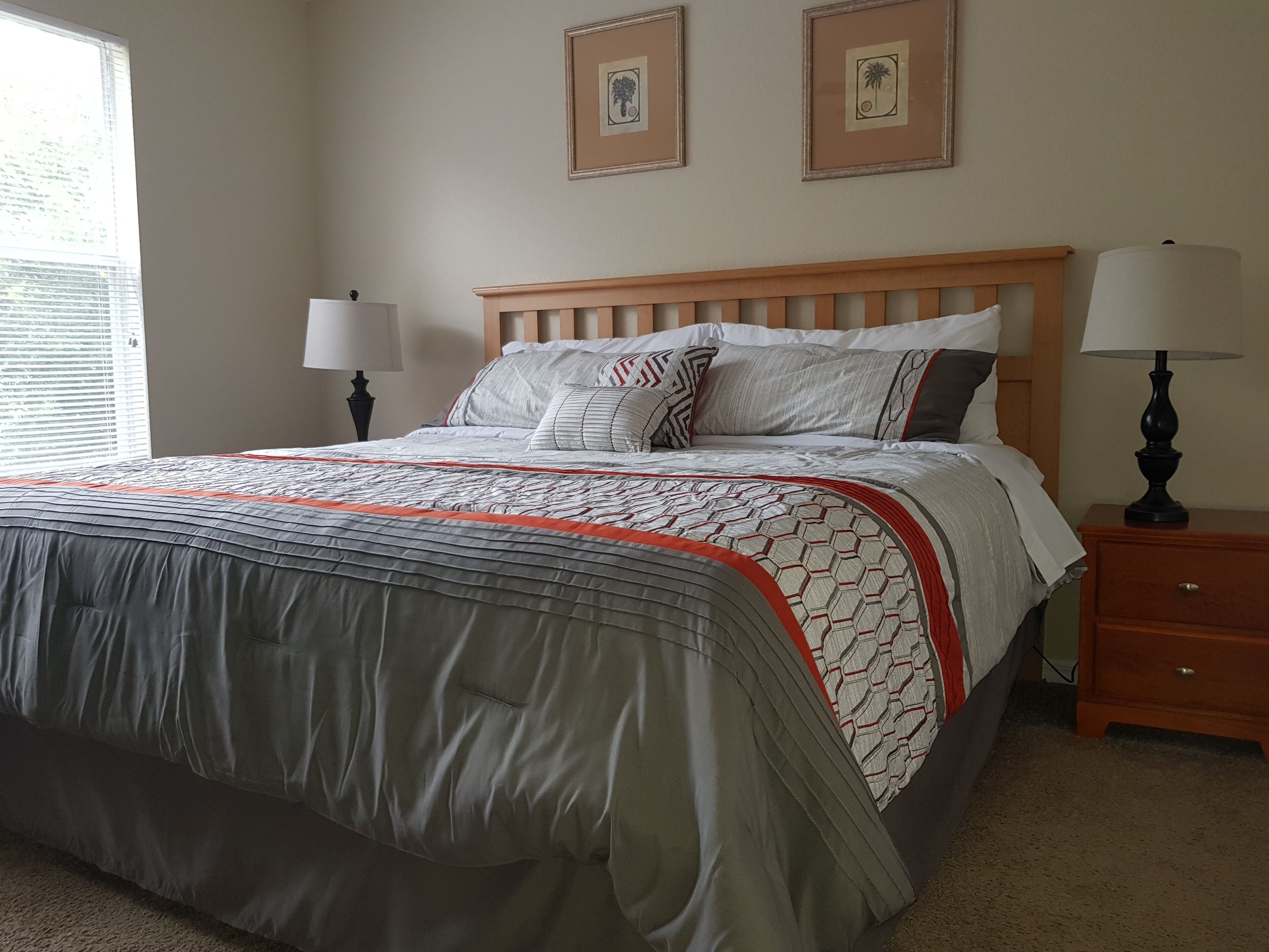 A neatly made bed with a patterned bedspread, two bedside lamps, and framed pictures on the wall.