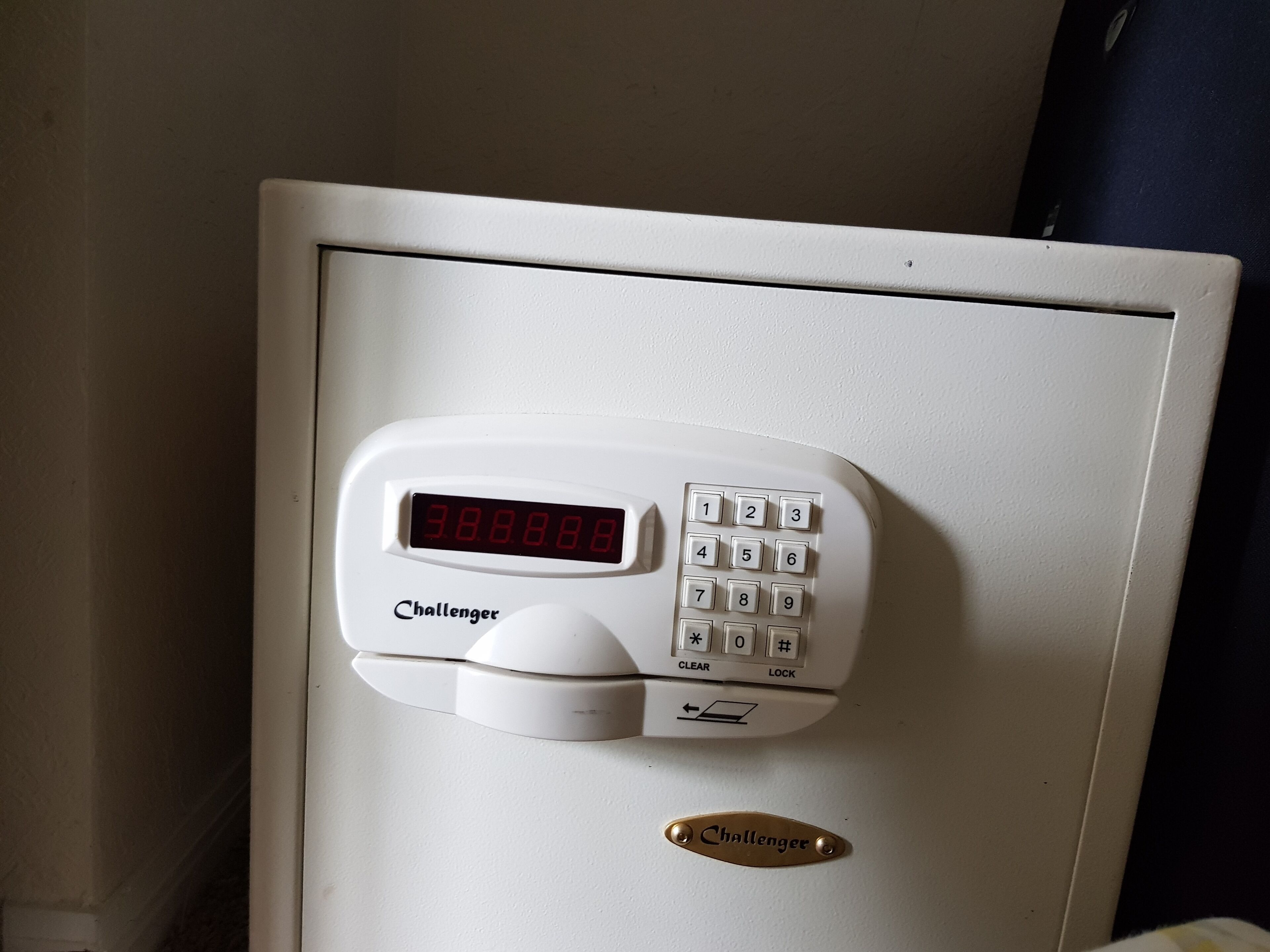 A white electronic keypad with a digital display on a white cabinet.