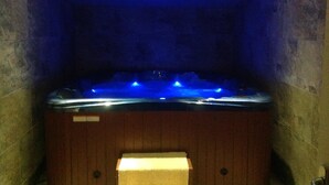 Een hottub met blauwe verlichting, houten wanden en een ventilatie rooster aan het plafond.
