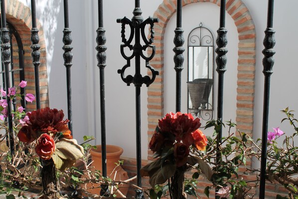 A courtyard with wrought iron fencing, terracotta pots, and potted plants with flowers.