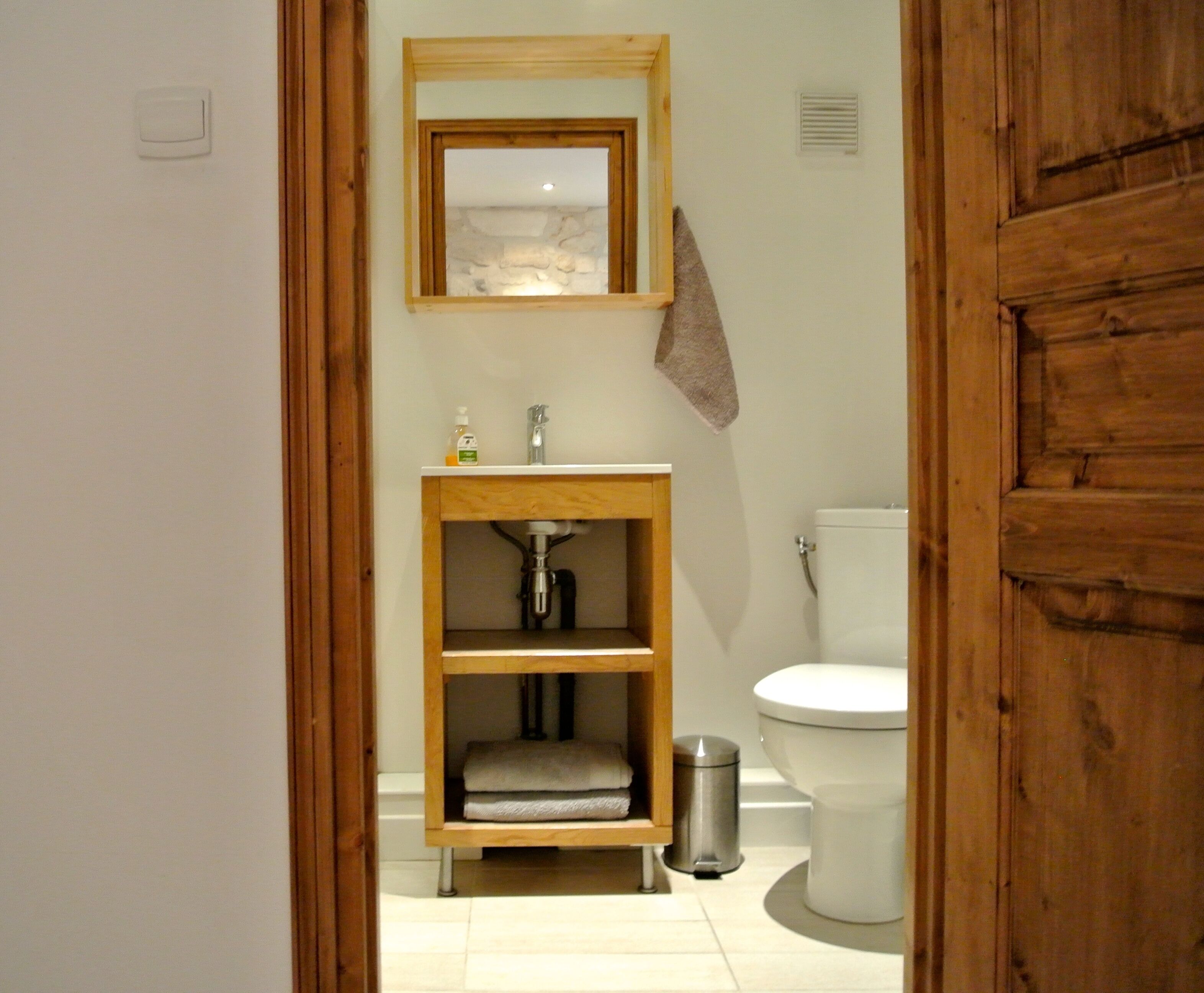 A bathroom with a wooden vanity, a sink, a mirror, a towel hanging on the wall, and a toilet.