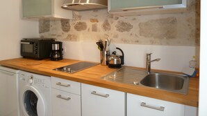 Een kleine keuken met een wasmachine, magnetron, koffiezetapparaat, waterkoker en een roestvrijstalen spoelbak.