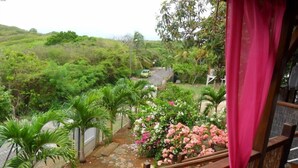 A balcony with a view of a garden, a stone pathway, and a green car in the background. - Gosier Charming bungalow facing the sea (Le Gosier)