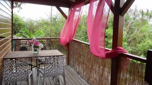 A wooden deck with a table and chairs, a pink curtain, and a view of greenery. - Gosier Charming bungalow facing the sea (Le Gosier)