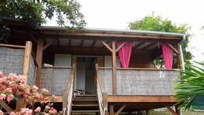 A wooden cabin with a porch, a staircase, and pink curtains. - Gosier Charming bungalow facing the sea (Le Gosier)
