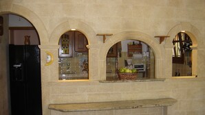 Une cuisine aux murs en pierre, avec un réfrigérateur noir et une fenêtre ornée d’un panier de pommes.