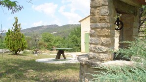 Un bâtiment en pierre avec une porte verte, une table en pierre avec un plateau vert et un arbre au premier plan.