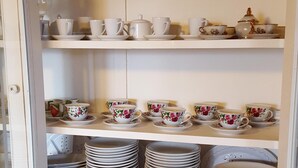 A kitchen with white cabinetry, a sink, and a countertop. There are several white cups and saucers on the shelves, and a vase with flowers on the countertop. - BEAUTIFUL VILLA WITH PRIVATE POOL, 150 METERS FROM THE SEA (QUARTU SANT'ELENA ,CAPITANA)