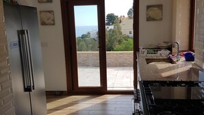 A kitchen with a modern stove, a refrigerator, and a view through the glass door to the outside.