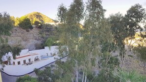 A white building with a swimming pool, surrounded by trees and hills.