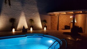 A swimming pool with a stone wall and potted plants in the background.