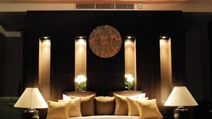 Un llit gran amb capçalera, dues làmpades laterals i un ventilador de sostre en una habitació poc il·luminada, amb una paret de fusta fosca i una obra d'art circular sobre el llit.