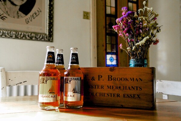 Three bottles of Whitstable Bay Organic Ale and Pale Ale, a wooden box labeled T. & P. Brookman Oyster Merchants, and a vase with flowers. - The Cook's Cottage: a coastal oasis w/outdoor kitchen, garden & cinema nr beach (Whitstable)
