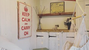 A cozy room with a wooden ceiling, a vintage stove, a hanging chair, and a 'KEEP CALM AND CARRY ON' sign. -  The Cook's Cottage: a coastal oasis w/outdoor kitchen, garden & cinema nr beach (Whitstable)