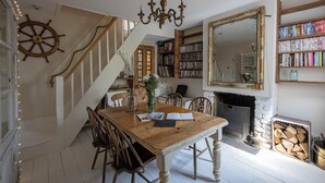 A dining area with a wooden table, chairs, a chandelier, a bookshelf, and a fireplace. -  The Cook's Cottage: a coastal oasis w/outdoor kitchen, garden & cinema nr beach (Whitstable)
