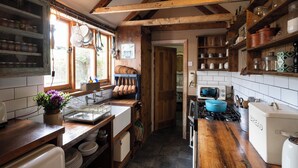 A rustic kitchen with wooden beams, a sink, a stove, and various kitchen utensils. -  The Cook's Cottage: a coastal oasis w/outdoor kitchen, garden & cinema nr beach (Whitstable)