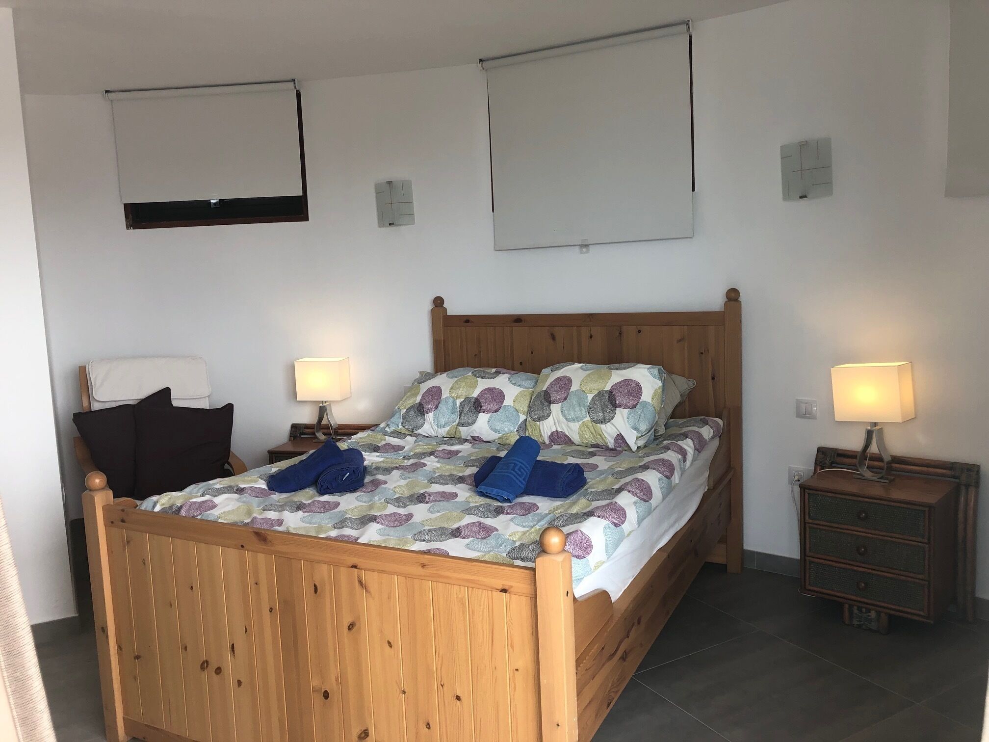 A wooden bed with a colorful bedspread, two bedside tables with lamps, and a small dresser.