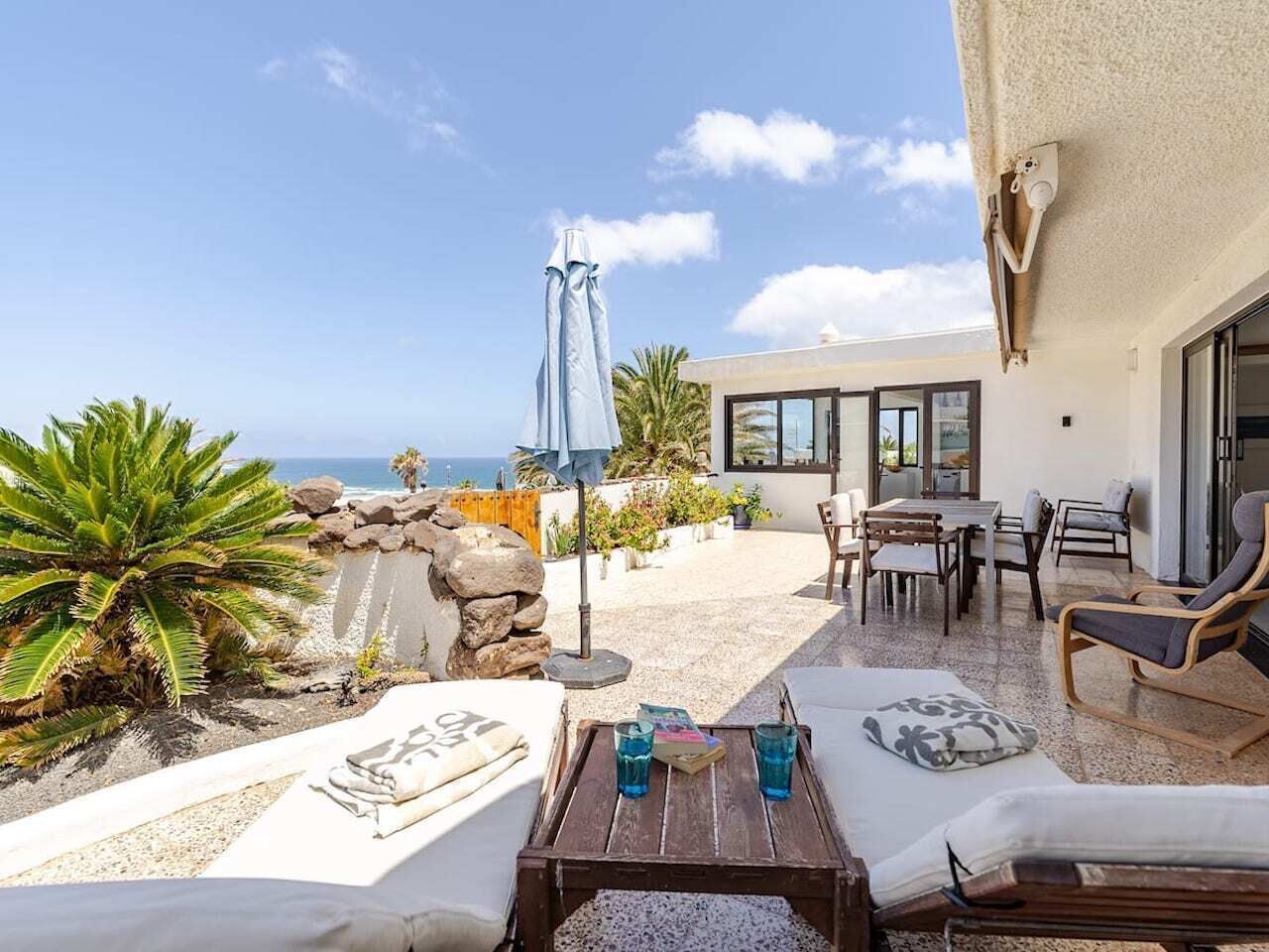 Une terrasse ensoleillée avec des chaises longues, une table avec des boissons et une vue sur la mer.