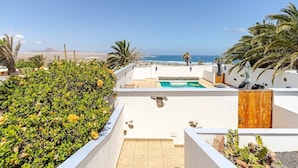 A rooftop pool with a view of the ocean, surrounded by greenery and palm trees. - Stunning beach view, heated pool, perfect house for comfort and relaxation   (Urbanización Famara)