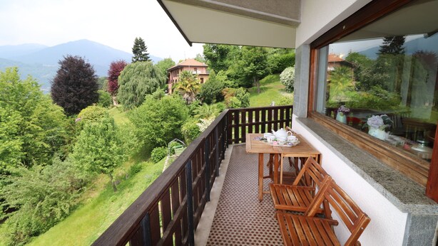 Een balkon met een houten tafel en stoelen, met uitzicht op een weelderige tuin en verre bergen.