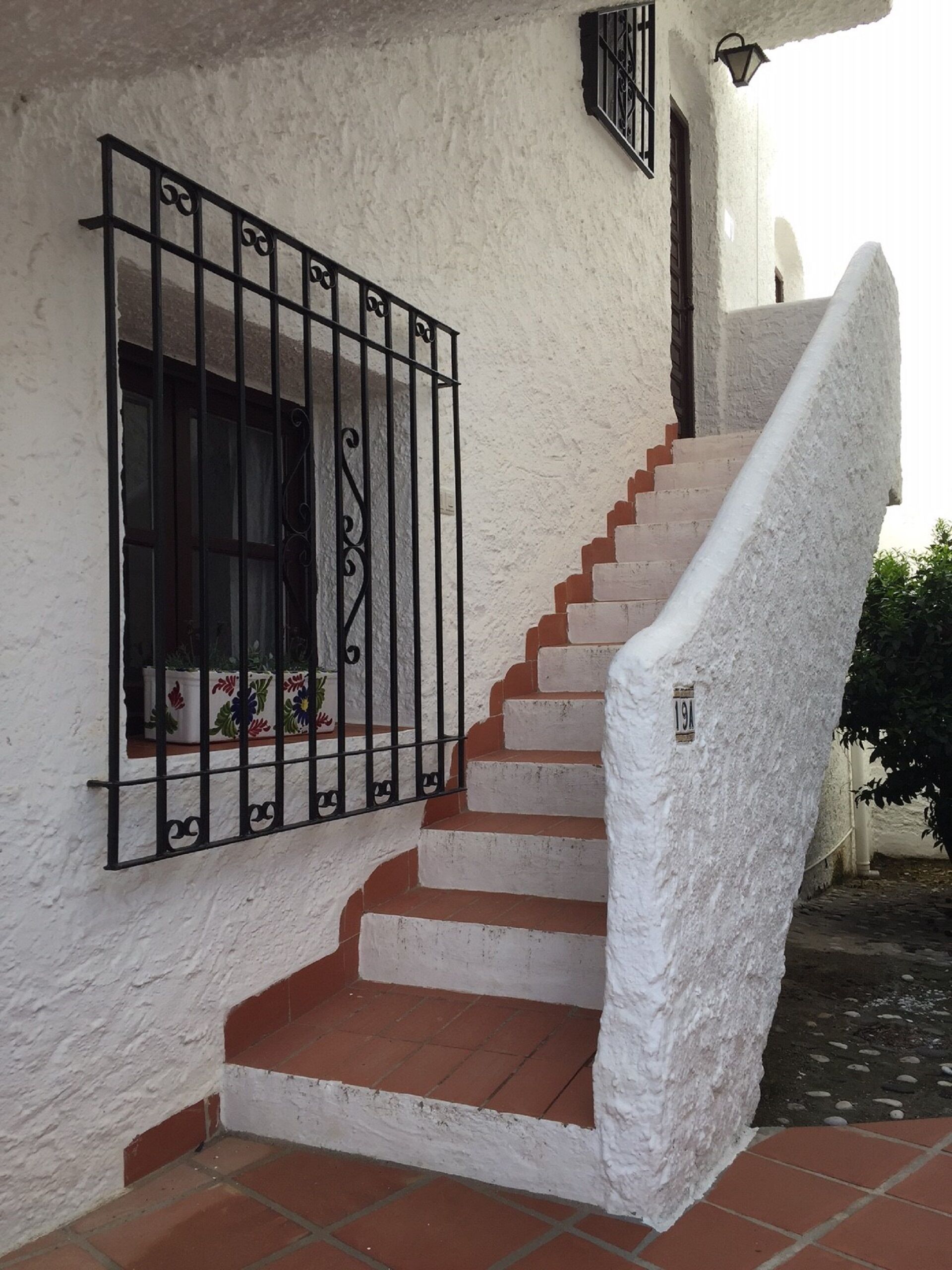 A staircase with white walls and red steps leading to a window with black metal bars.
