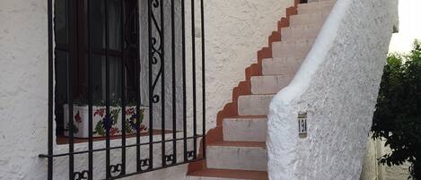 A staircase with white walls and red steps leading to a window with black metal bars.