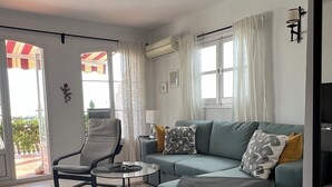 Un salon comprenant un canapé, un fauteuil, une table basse et une vue sur l’extérieur, visible à travers une porte vitrée.
