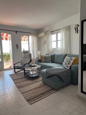 A living room with a sofa, armchair, coffee table, and a view through a glass door.