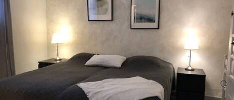 A bedroom with a large bed, two bedside tables with lamps, and two framed pictures on the wall.