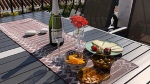 Une terrasse avec une table dressée pour un repas, une bouteille de vin et un vase rempli de fleurs.