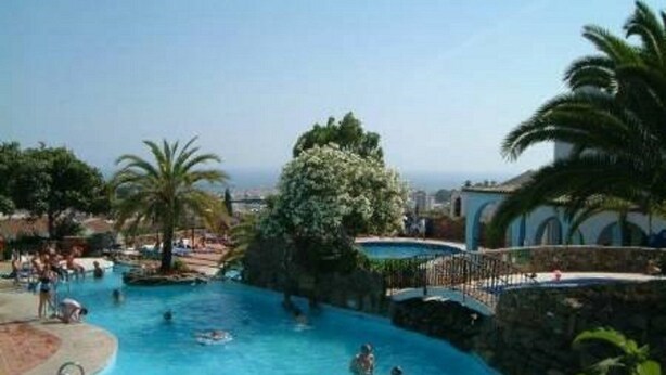 Une piscine où se baignent des gens, entourée de palmiers et offrant une vue sur la ville.