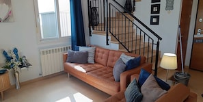 Een woonkamer met een bruine leren bank, een lamp en een trap.