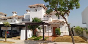A multi-story residential building with a covered parking area, a small garden, and a palm tree.