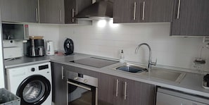 A compact kitchen with a washing machine, a coffee maker, a kettle, and a sink.