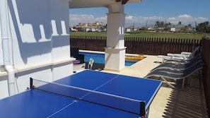A pool area with a ping pong table, lounge chairs, and a wooden fence.