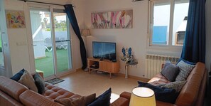 A living room with a television, a sofa, a coffee table, and a view of a garden through a sliding door.