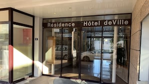 A hotel entrance with a glass door, a sign reading "Résidence Hôtel de Ville", and a car parked outside.