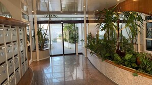 A modern lobby with a polished floor, a reception desk, and a plant-filled area.