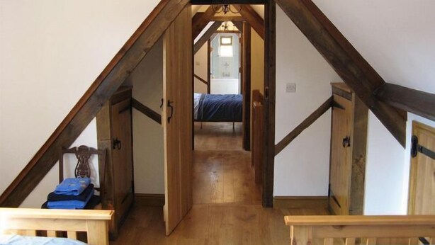 A bedroom with a sloped ceiling, wooden beams, a bed, and a small table with a lamp.