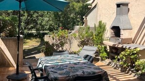 Un patio esterno con tavolo e sedie, un ombrello verde e un camino in pietra.